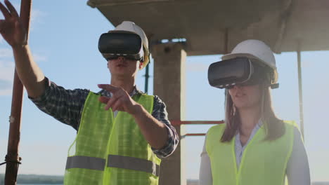 A-man-and-a-woman-engineers-at-a-construction-site-in-VR-glasses-manage-the-construction-of-a-building-discussing-a-development-plan
